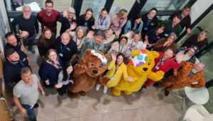 Pudsy bear and blush with a group of Two Rivers Housing team members looking up to the camera and cheering