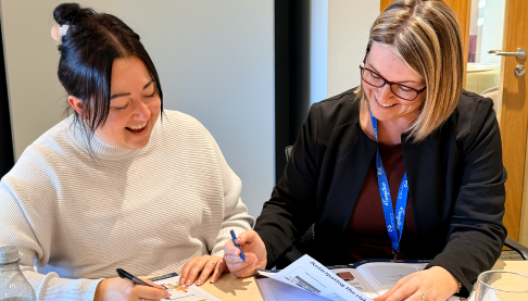 Two team members in a training workshop, holding pens and discussing a task