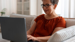 Woman sat on her sofa using a laptop to access information.